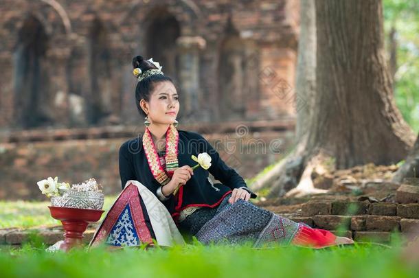 年幼的亚洲人女人采用传统的衣服坐向绿色的草和英语字母表的第16个字母