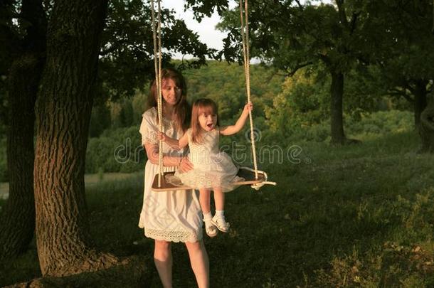 妈妈颤抖她女儿向摇摆在下面一树采用太阳.关-在上面.