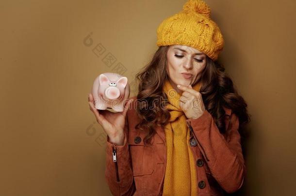 沉思的时髦的女人和小猪银行向米黄色背景