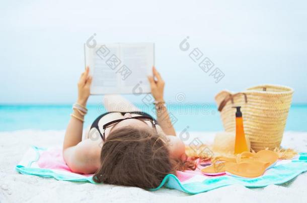 中部年龄女人向白色的海滩阅读书在期间产卵数