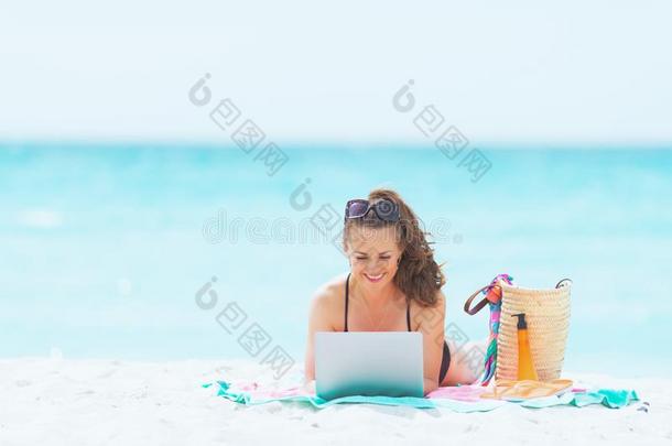 幸福的时髦的40年老的女人向白色的海滩使用互联网