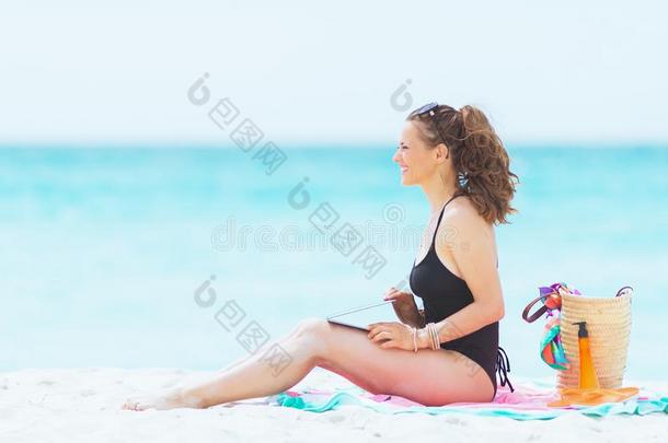 幸福的时髦的40年老的女人向白色的海滩和便携式电脑