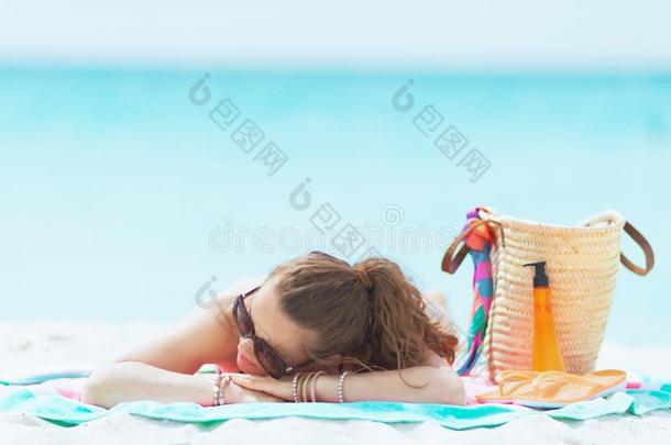 轻松的时髦的40年老的女人向白色的海滩睡眠