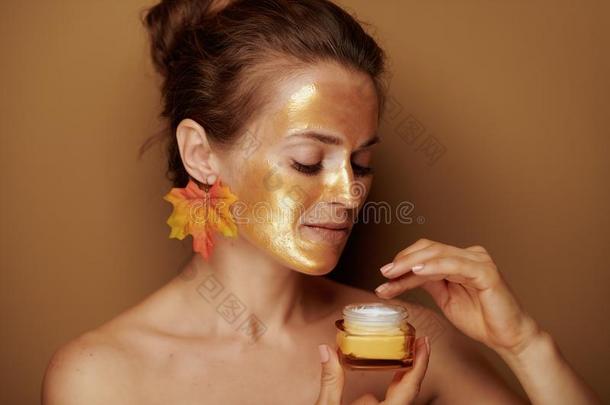 现代的家庭主妇和金色的面具使用化妆品产品