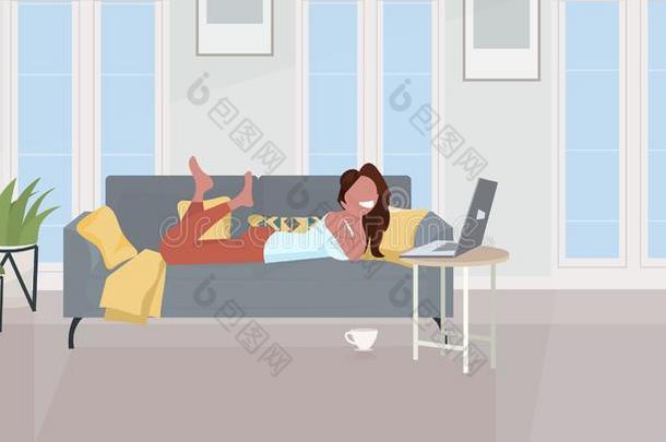 女孩说谎向沙发使用便携式电脑幸福的女人令人轻松的在家摩登派