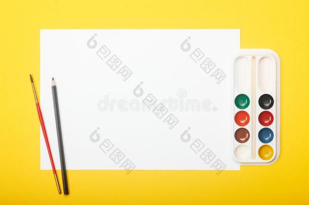 空白的纸和铅笔,刷子和绘画颜料向黄色的背景.