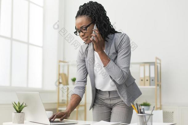 非洲式发型女士讲话向蜂窝式便携无线电话打字向便携式电脑采用办公室