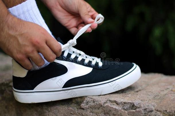 年幼的男孩系指已提到的人鞋带关于他的黑的和白色的旅游鞋采用