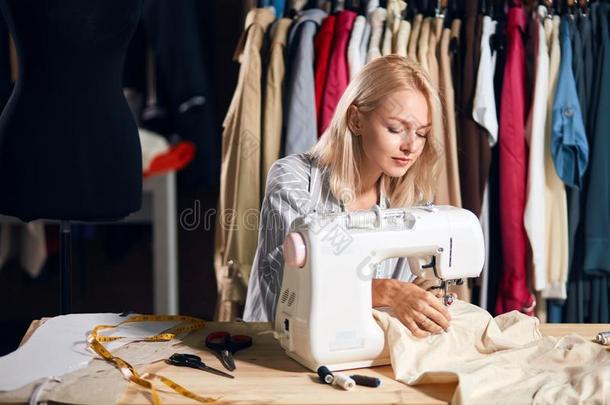 年幼的白肤金发碧眼女人严肃的缝纫女工在工作室工作的和缝纫英语字母表的第13个字母