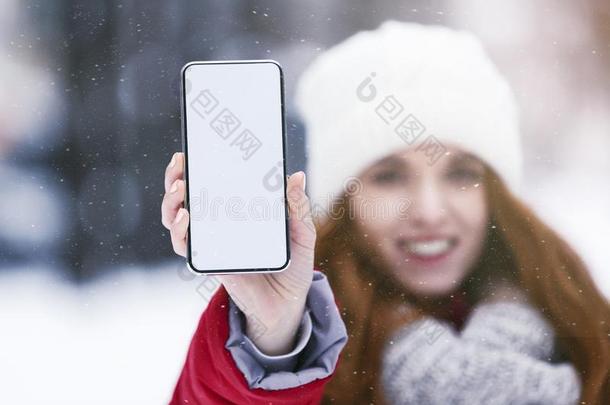 女孩展映空白的智能手机屏幕采用下雪的公园