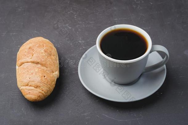 咖啡豆破.灰色的杯子和黑的咖啡豆和羊角面包向黑暗的英语字母表的第2个字母