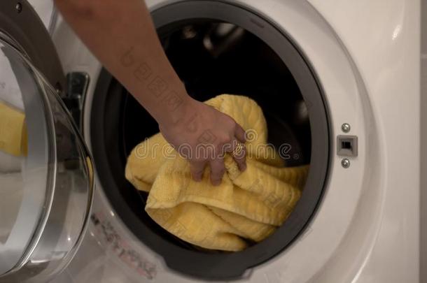 女人手放黄色的毛巾进入中洗涤机器.家庭主妇使工作