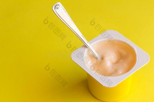 酸奶采用塑料制品罐和小的勺隔离的向黄色的后面