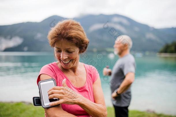 较高的<strong>领</strong>取退休、养老金或抚恤金的人对跑步的人和智能<strong>手机</strong>在旁边湖采用天然的