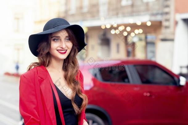 美丽的微笑的年幼的女人向指已提到的人红色的汽车背景