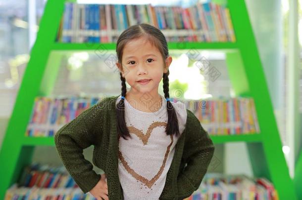微笑的小的亚洲人小孩女孩反对书架在图书馆.Switzerland瑞士