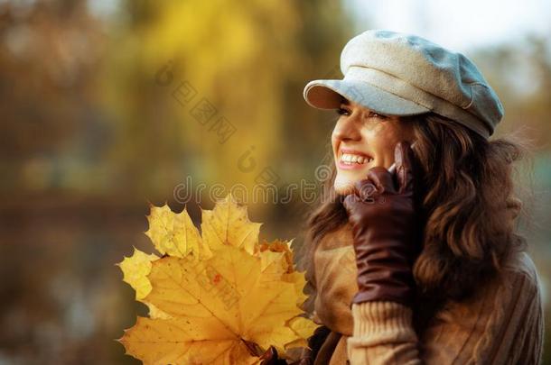 幸福的优美的女人和黄色的树叶使用智能手机