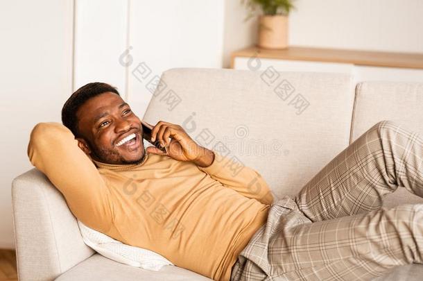 非洲式发型男人讲话向蜂窝式便携无线电话说谎向长沙发椅在家