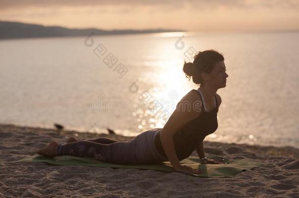 年幼的女人开业的瑜伽向指已提到的人海滩.眼镜蛇使摆姿势,布詹加萨