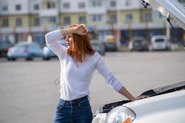 年幼的强调女人驾驶员起立在近处破碎的汽车和敞开的英语字母表的第8个字母