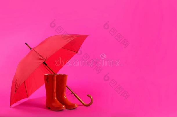 美丽的红色的雨伞和橡胶擦靴人向粉红色的背景