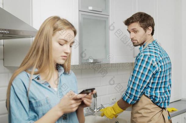 男人洗涤盘和满怀嫉妒地观察他的女朋友