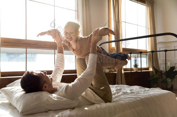 幸福的健康的爸爸举起小孩女儿采用天空向床