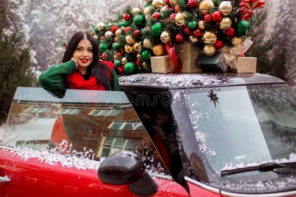 漂亮的年幼的女孩是（be的三单形式起立在近处红色的汽车和装饰圣诞节英语字母表的第20个字母