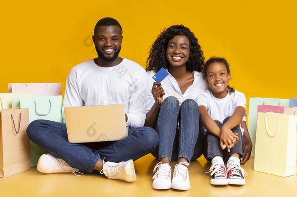 快乐的非洲式发型家庭和便携式电脑,信誉卡片和购物袋.