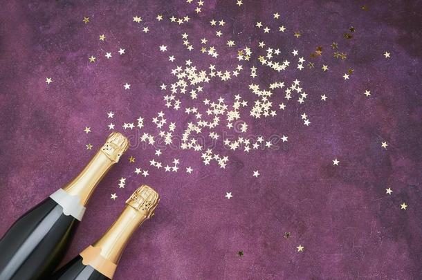两个香槟酒瓶子和金色的五彩纸屑向紫色的背景.