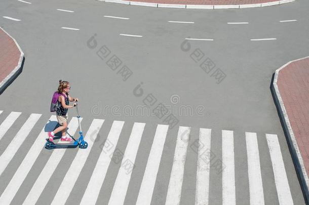 女孩运送的小型摩托车和人行横道路向道路向学校.斑马