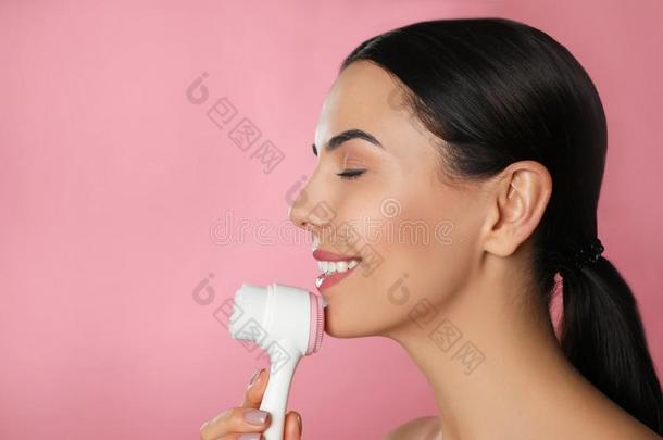 年幼的女人使用面部的清洁刷子向粉红色的背景,休闲健身中心
