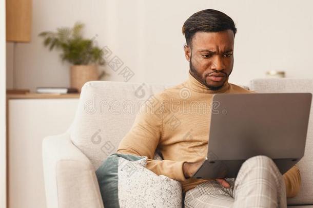 黑的家伙使用便携式电脑工作的一次向长沙发椅在家