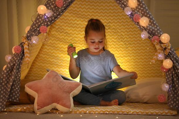 小的女孩和手电筒阅读书采用比赛帐篷