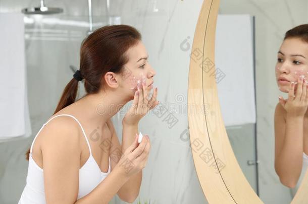 青少年女孩和痤疮问题应用乳霜在近处镜子