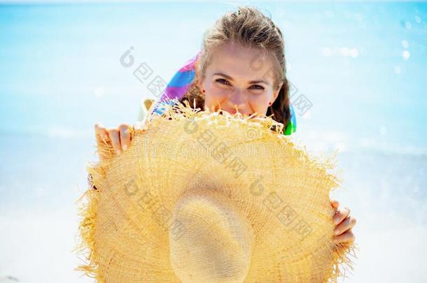 幸福的现代的女人躲藏在的后面和大的稻草帽子向海岸