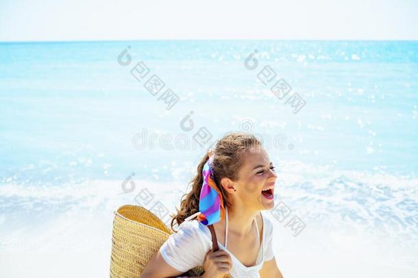 微笑的现代的女人和海滩稻草袋跑步向海岸