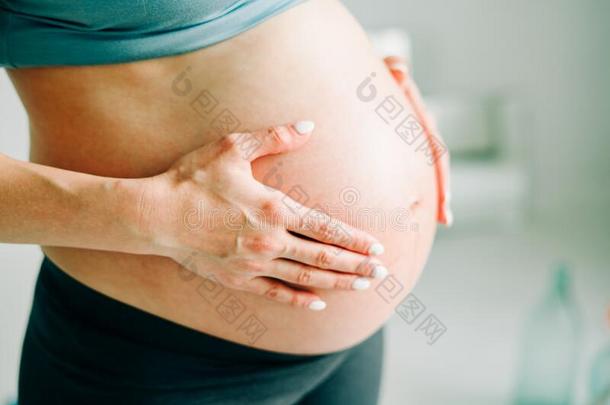怀孕的女孩采用运动装紧抱她光秃秃的肚子采用指已提到的人工作室
