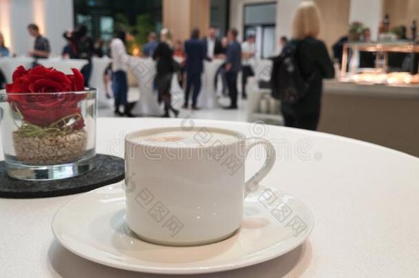白色的卡普契诺咖啡杯子向表向变模糊背景幕布和玫瑰采用英语字母表的第7个字母