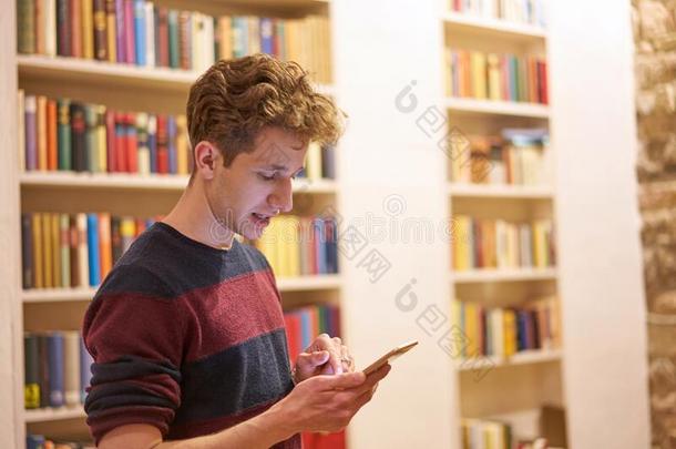 年幼的学生采用图书馆用途他的电话采用前面关于书架