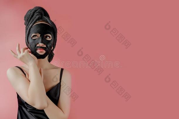 年幼的女人应用黑的化妆品织物面部的面具向粉红色的背