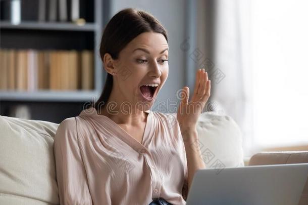 吃惊的年幼的女人有样子的在便携式电脑屏幕,静止的向沙发.