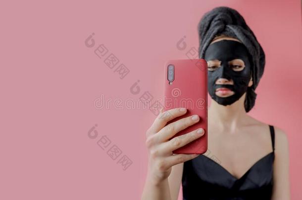 年幼的女人应用黑的化妆品织物面部的面具和电话采用