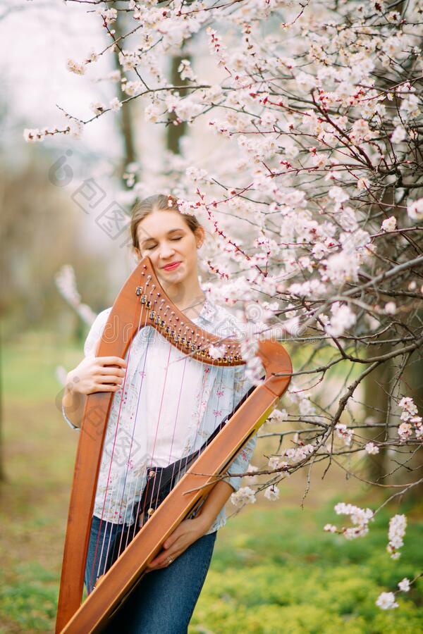 女人弹竖琴者有享有在开花花园和演奏竖琴图片-包图网企业站