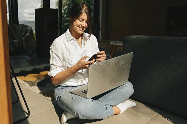 幸福的时髦的女孩闲谈向ph向e和使用便携式电脑在期间sitting-room起居室