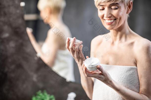 微笑的女人开幕面部的乳霜起立采用浴室在家