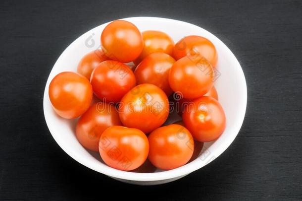 红色的小的樱桃番茄采用白色的碗向黑的木制的背景