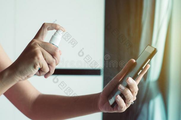 女人手使用喷雾乙醇向智能手机,预防measure量度