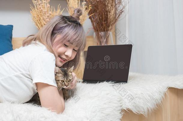 幸福的年幼的亚洲人女人和便携式电脑计算机<strong>抚摸</strong>小猫莱伊