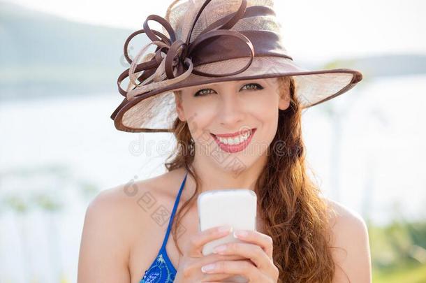 微笑的美丽的女人采用帽子和智能手机look采用g在照相机
